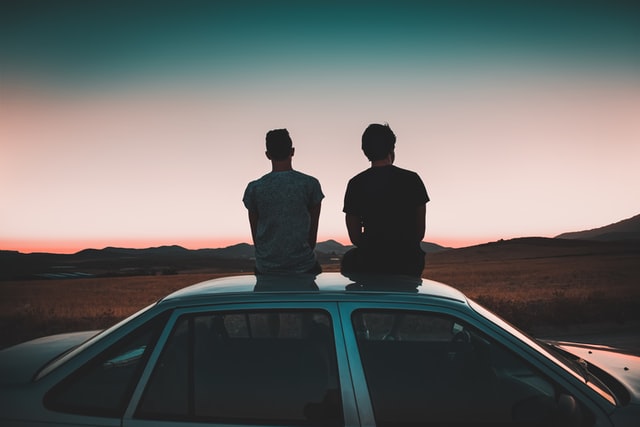 Two men sitting on the roof of a car watching the sunset. Picture used for a tale of two brothers in Jayanthy's Free Space.